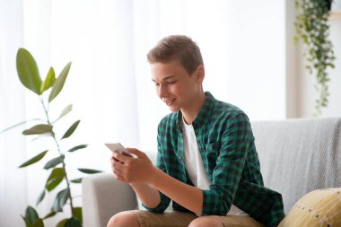 Evdeki kanepede oturan ve cep telefonu kullanan bir genç.