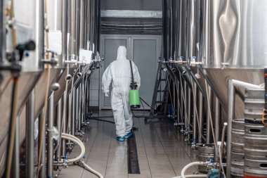 Fabrika dezenfeksiyonu. Koruyucu kıyafetli bir işçi, bira fabrikasını temizliyor.