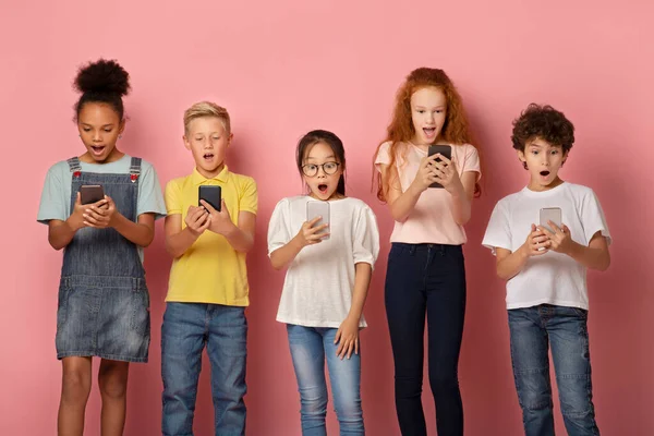 Écoliers choqués regardant dans leurs téléphones mobiles sur fond rose — Photo
