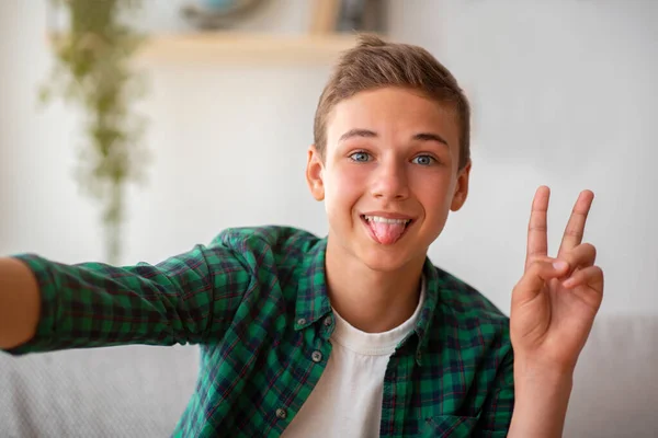 Söt tonåring pojke som tar selfie, visar tunga och fred gest — Stockfoto