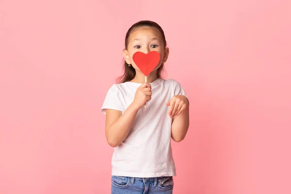 Азійська дівчинка тримає паперове серце біля рота. — стокове фото