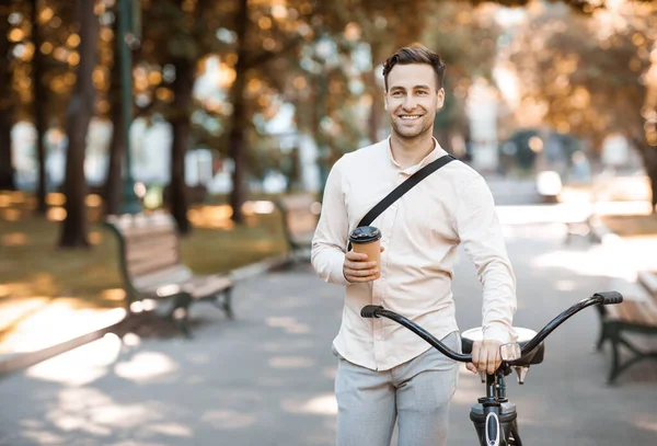 Andiamo in ufficio. Ragazzo sorridente con tazza di caffè che cammina con la bici — Foto Stock