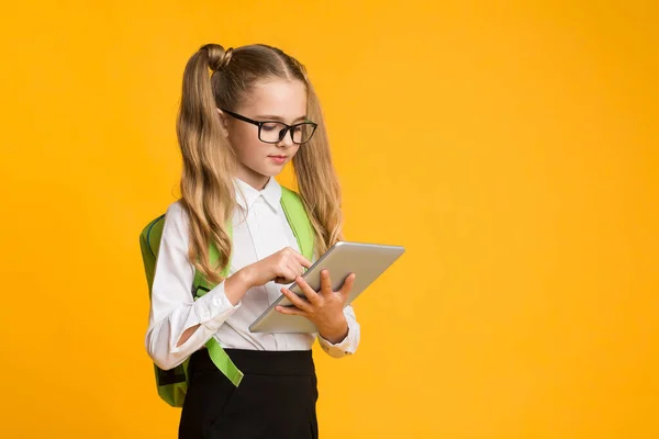 Školačka pomocí tabletu počítače dělat školní domácí úkol stojící ve studiu — Stock fotografie