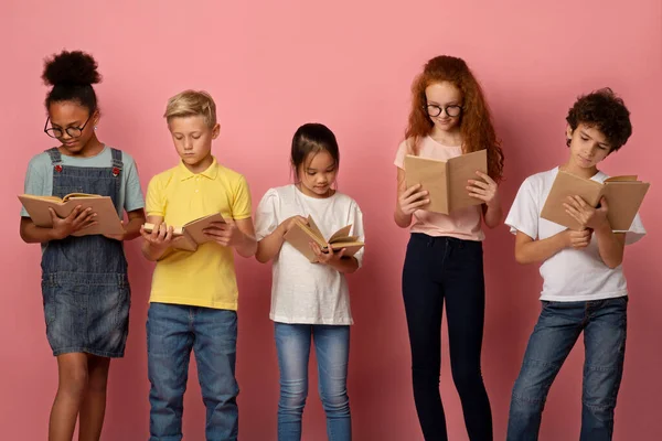 Niños industriosos y diversos leyendo libros de texto escolares sobre fondo rosa —  Fotos de Stock