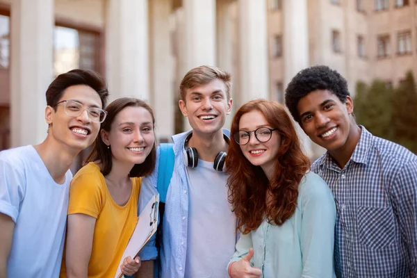 Alegre multiétnicos estudiantes posando sonriendo a la cámara de pie fuera de la universidad —  Fotos de Stock
