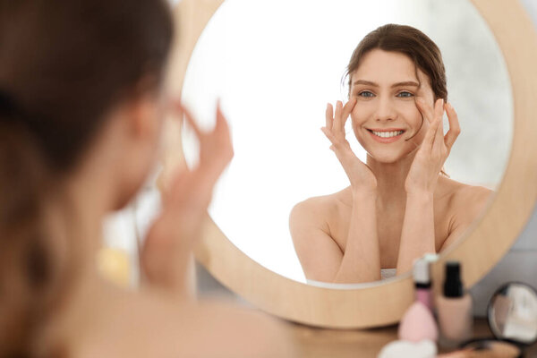 Young woman massaging eye zone, looking at mirror