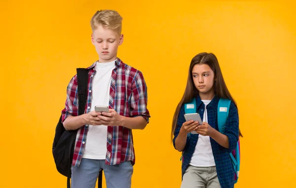 Casual schoolkinderen staan met telefoons op gele studio — Stockfoto