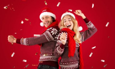 Neşeli milenyum çifti Noel 'de ya da yeni yıl partisinde kırmızı arka planda dans ediyor ve konfeti düşüyor.