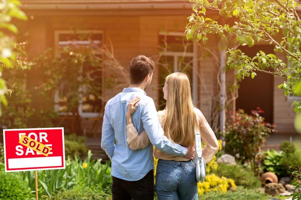 Back view of young couple standing in front yard of their new house, outside