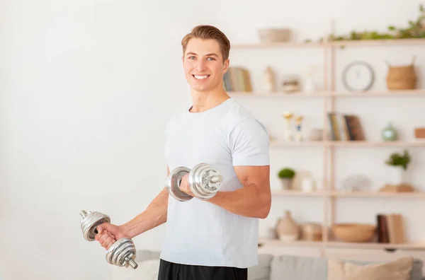 Krachttraining thuis tijdens quarantaine. Lachende knappe man tilt halters — Stockfoto