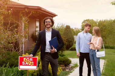 Kendine güvenen emlakçı ve dışarıda güzel bir kır evinin yakınında mutlu genç bir çift.