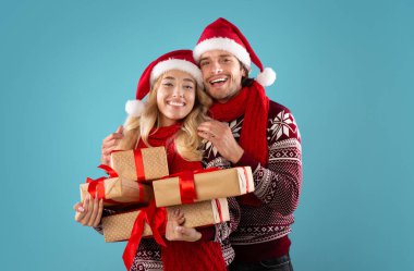 Yeni yıl hediyeleriyle romantik bir çift mavi arka planda sarılıyor ve gülümsüyor.
