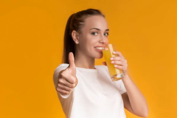 Mujer joven bebiendo jugo saludable y mostrando gesto de pulgar hacia arriba — Foto de Stock