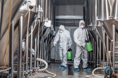 Tehlikeli madde giysisi içindeki işçiler bira fabrikasında dezenfeksiyon yapıyor.
