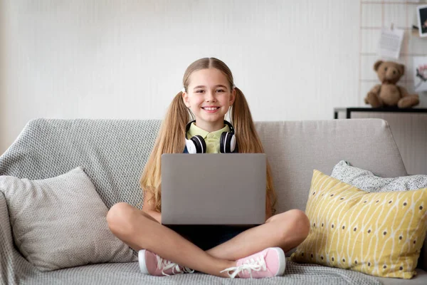 女孩坐在沙发上，用笔记本电脑 — 图库照片