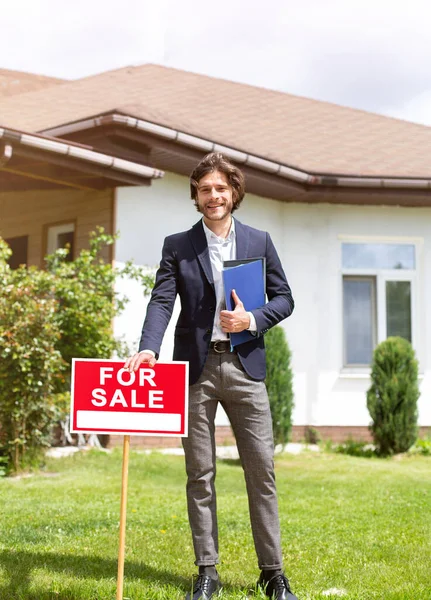 Full length portrait of property manager standing near FOR SALE sign in front of new building outdoors — Stock Photo, Image