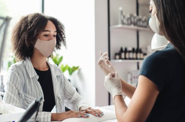 Asyalı uzman koruyucu maskeli Afrikalı Amerikalı müşteriyle çalışıyor.