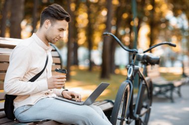 Çevre taşımacılığı ve şehirde çalışmak. Genç adam dizüstü bilgisayarda çalışıyor ve bankta kahve içiyor.