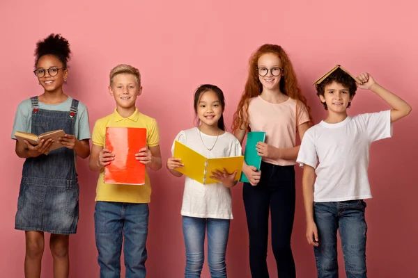 Cool niños y niñas con libros de texto de la escuela y copybooks posando sobre fondo rosa —  Fotos de Stock