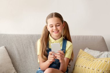 Kanepede oturan kız cep telefonunu kullanıyor.