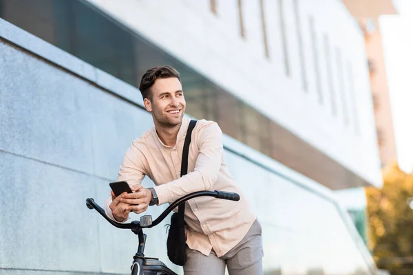 Homem alegre posa com bicicleta. Jovem hipster com smartphone perto do edifício — Fotografia de Stock