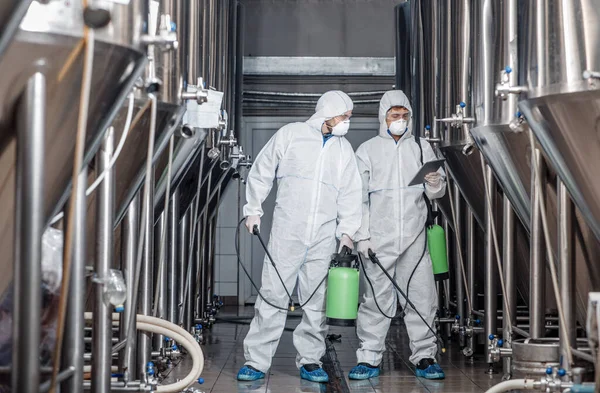 Los tipos con trajes de materiales peligrosos y máscaras desinfectan las teteras de la fábrica de cerveza en la planta artesanal — Foto de Stock