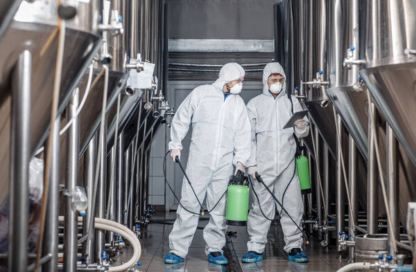 Guys in hazmat suits and masks disinfect brewery kettles at craft plant