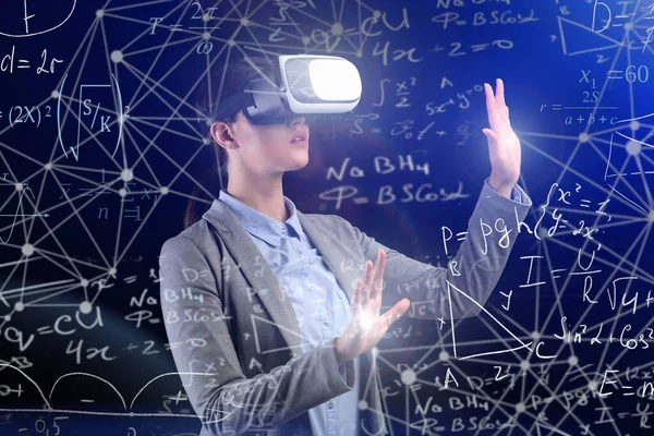 Mulher vestindo óculos de realidade virtual aprendendo fórmulas científicas, fundo azul — Fotografia de Stock