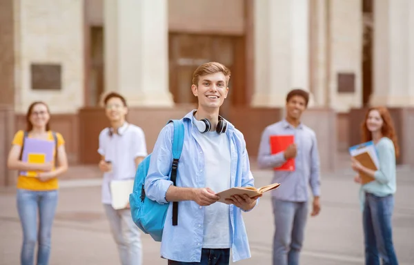 Alegre millennial chico de pie entre multiétnicos estudiantes cerca de la universidad al aire libre — Foto de Stock