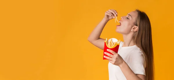 Giovane donna che mangia patate fritte francesi su sfondo giallo Studio — Foto Stock