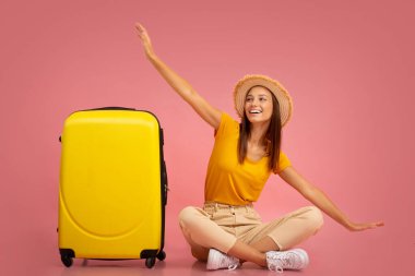 Bavulun yanında oturan kız, uçak taklidi yapıyor.