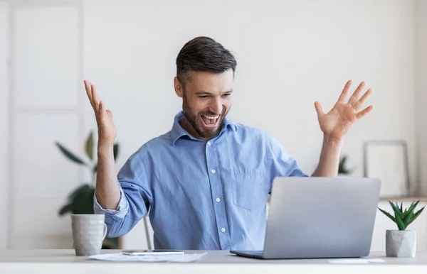 Счастливый предприниматель-мужчина эмоционально празднует успех бизнеса с ноутбуком в офисе — стоковое фото