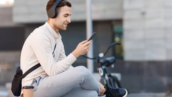Сучасні онлайн-технології. Усміхнений хлопець в навушниках з велосипедом дивиться на смартфон — стокове фото