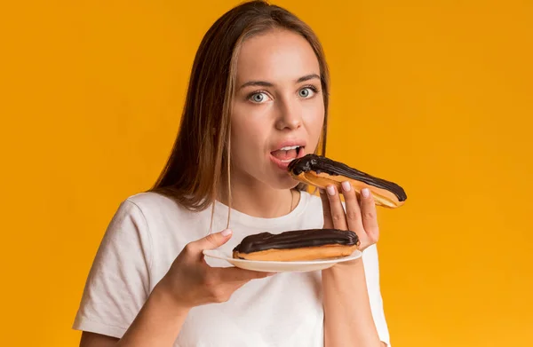 Milenyum Kızı Çikolatalı Eklemenin Tadını Çıkartıyor, Sarı Arkaplanda Sağlıksız Şekerler Yiyor — Stok fotoğraf