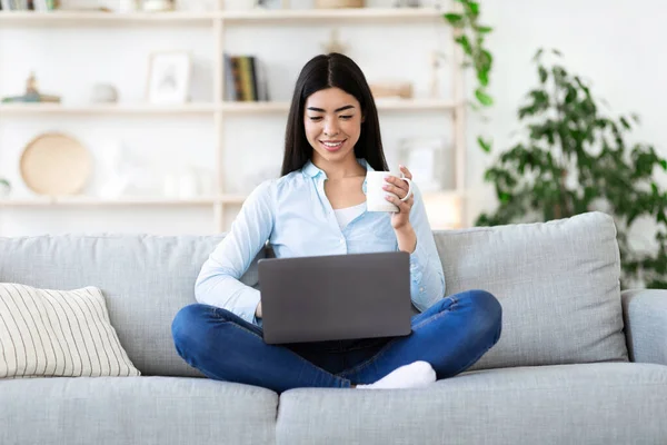 Concepto de ocio. Chica asiática relajarse en el sofá, beber café y usar el ordenador portátil — Foto de Stock