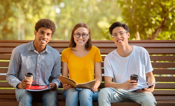 Üç öğrenci bankta oturmuş, dışarıda kahve içiyorlar. — Stok fotoğraf