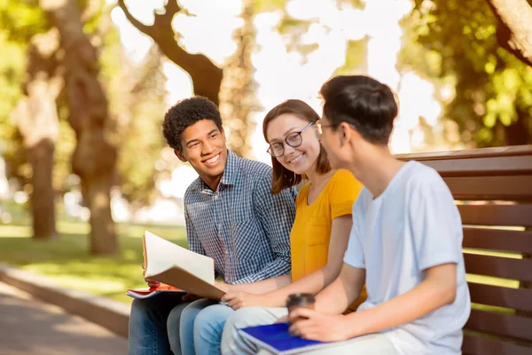 Üç öğrenci konuşuyor, sınıfları tartışıyorlar, bankta oturup dinleniyorlar. — Stok fotoğraf
