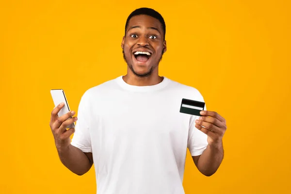 신용 카드와 전화를 든 행복 한 아프리카 남자, 노란 배경 — 스톡 사진