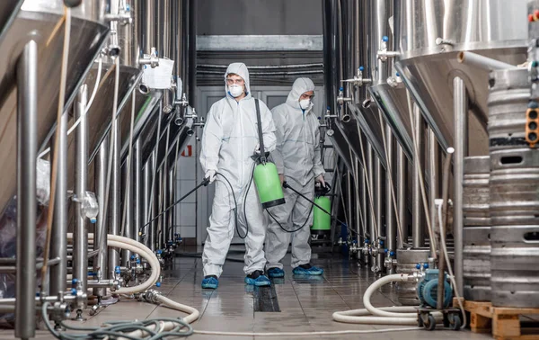 Cuarentena y prevención en fábrica. Hombre en traje protector desinfecta teteras de cerveza — Foto de Stock
