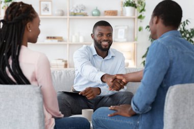 Başarılı bir toplantının ardından minnettar siyah çift ve evlilik terapisti el sıkışıyor.