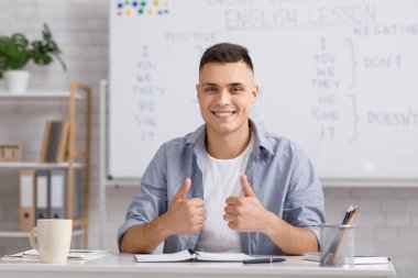 Uzaktan öğrenme dili. Gülümseyen genç erkek öğretmen öğrencilere İngilizce kurallarını anlatıyor.