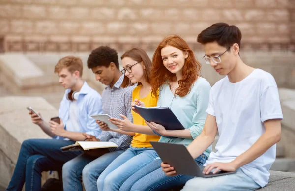 Chica aprendiendo con otros estudiantes sentados en el campus universitario —  Fotos de Stock