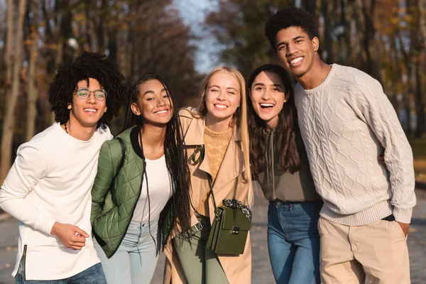 Adolescentes multiétnicos alegres abraçando e sorrindo para a câmera ao ar livre — Fotografia de Stock