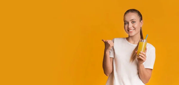 Mulher positiva posando com suco de vitamina laranja fresca e apontando para o lado — Fotografia de Stock