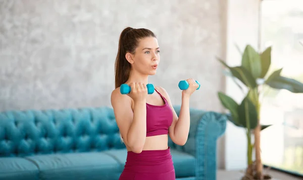 Konzentriertes junges Mädchen in Sportkleidung macht zu Hause Kraftübungen mit Kurzhanteln — Stockfoto