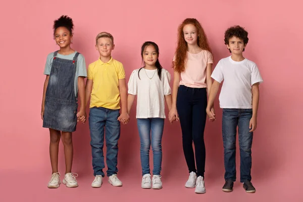 Amistad escolar. Adorables niños multiétnicos tomados de la mano sobre fondo rosa — Foto de Stock