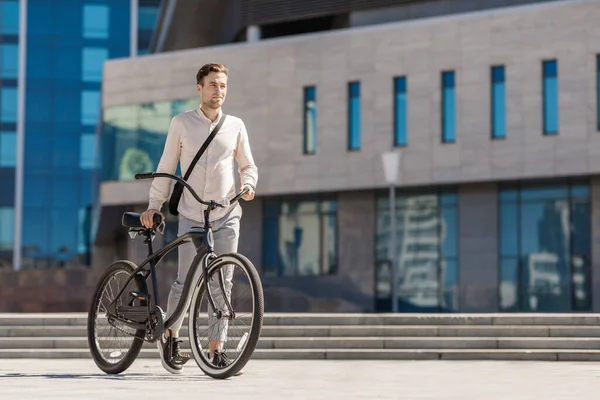 Jovem sorridente elegante empresário empurrando bicicleta enquanto vai trabalhar — Fotografia de Stock