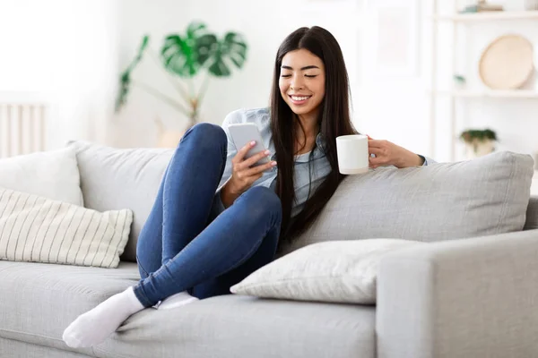 Fin de semana Relájate. Feliz chica asiática usando Smartphone y teniendo café de la mañana — Foto de Stock