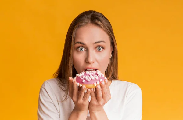 Jovem mulher mordendo saboroso donut, posando sobre fundo amarelo no estúdio — Fotografia de Stock