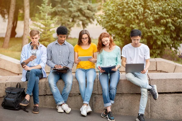 Estudantes aprendendo usando gadgets sentados ao ar livre no campus universitário — Fotografia de Stock